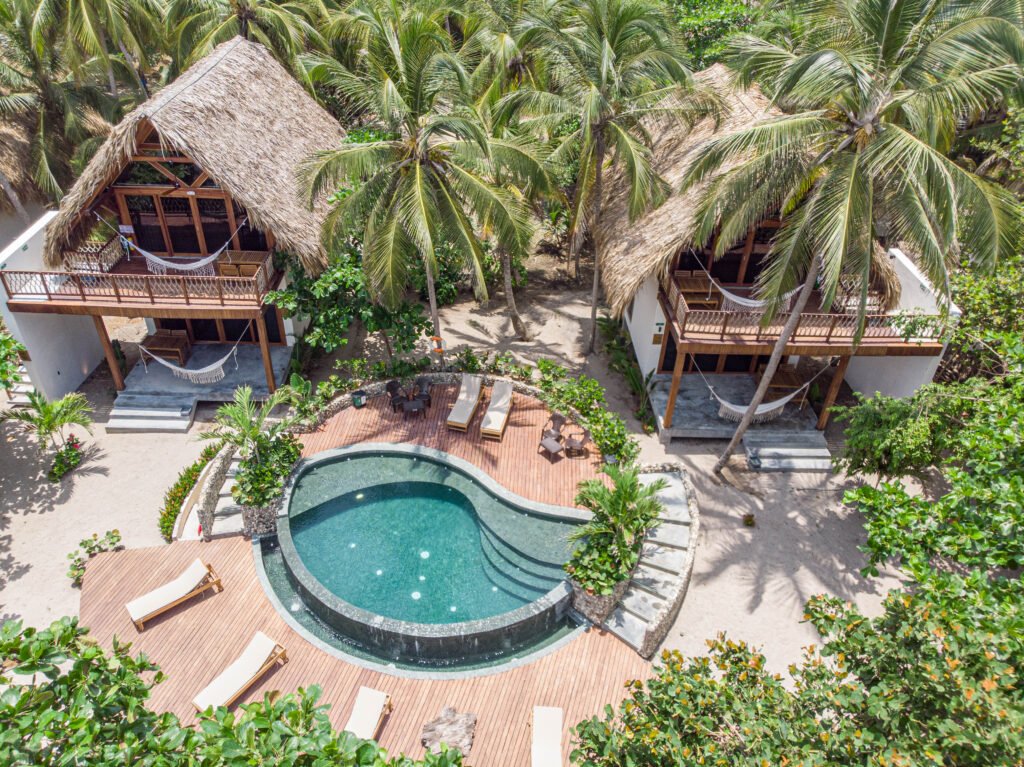 Vista aérea de las suites de Casa Iwana Tayrona con techos de palma, hamacas y piscina en primera línea de playa