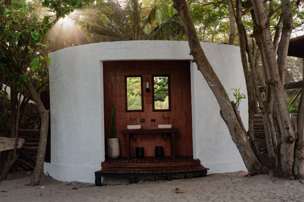Baño exterior redondo de Casa Iwana entre los árboles, con doble lavamanos
