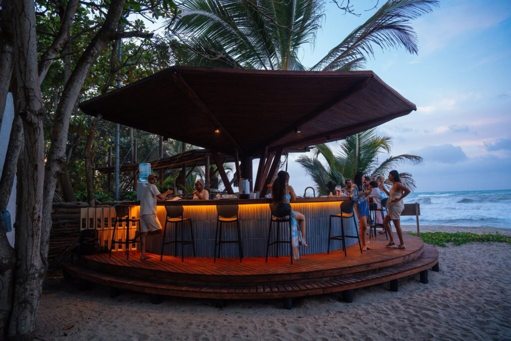 Gastrobar de Casa Iwana sobre la arena al atardecer, con huéspedes en la barra y el mar de fondo