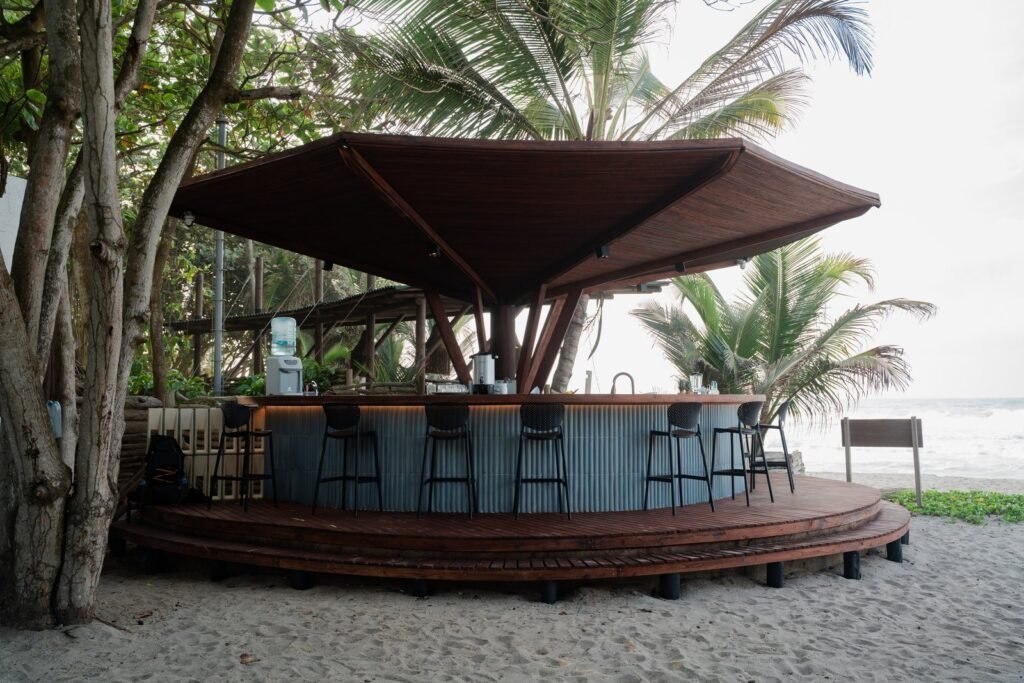 Gastrobar circular de Casa Iwana de día, con taburetes y palmeras junto a la playa