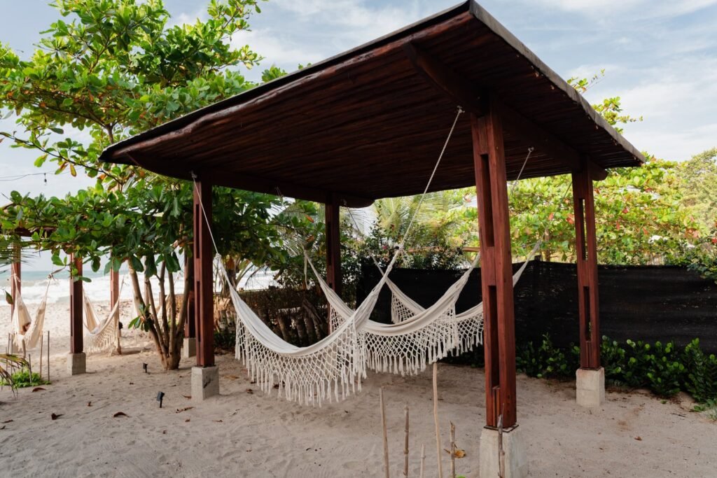 Pérgola con hamacas tejidas entre el jardín tropical y la playa de Casa Iwana